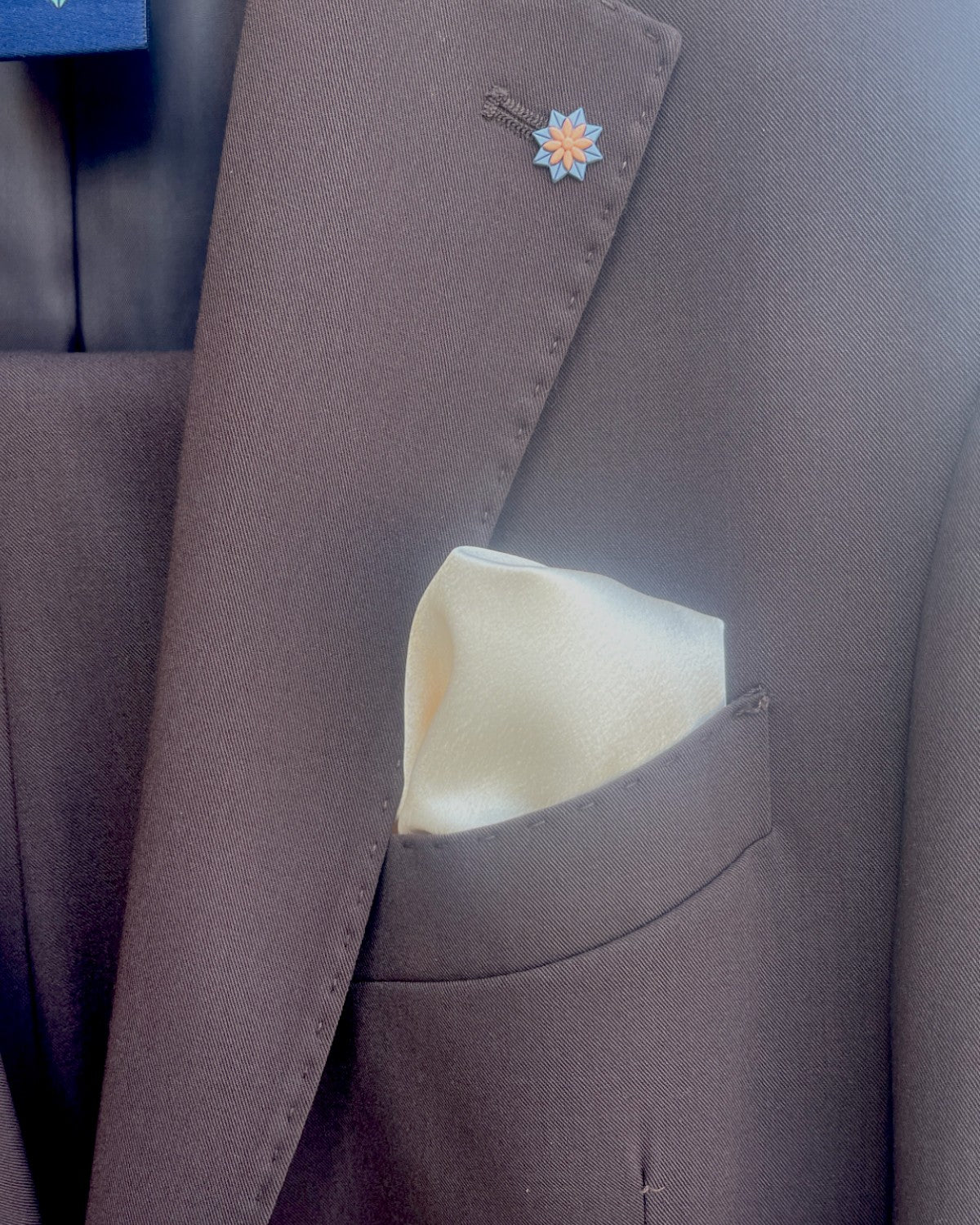 Particolare del taschino con pochette chiara e spilla floreale sulla giacca dell’Abito Uomo Kobe elegante in misto lana marrone.